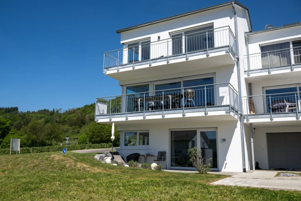 ferienhaus-aura-aussenansicht-balkone-seitenansicht Seitenansicht des Ferienhaus Aura mit drei Etagen, Balkonen und gruener Huegellandschaft im Hintergrund