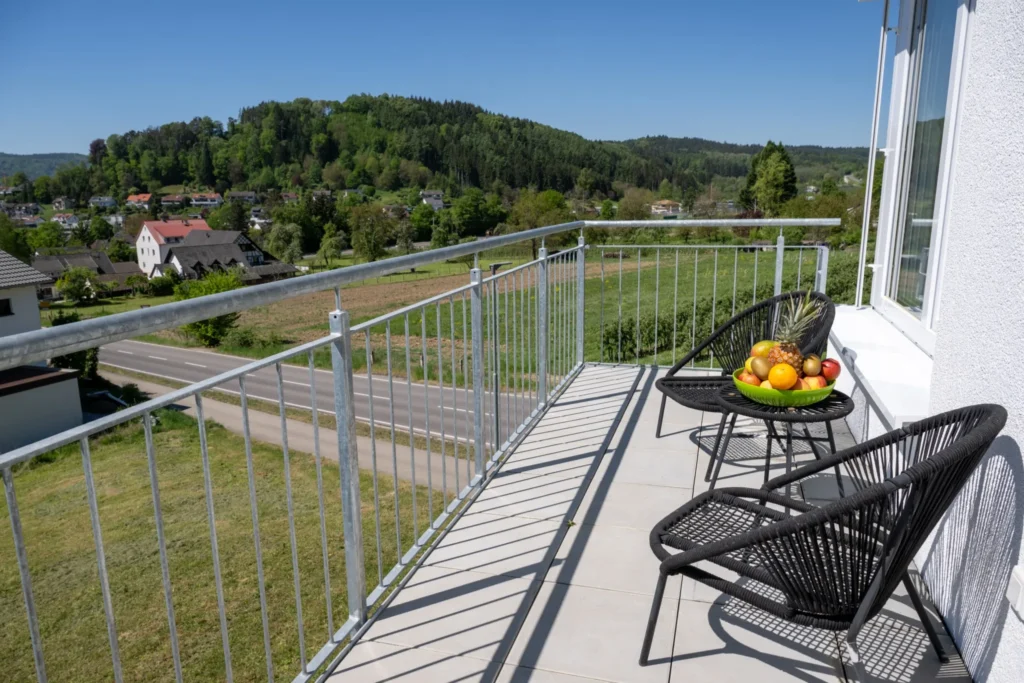 ferienhaus-aura-balkon-lounge-bergblick Seitenbalkon im Ferienhaus Aura mit Lounge-Stuehlen, Obstschale und Blick auf gruene Huegellandschaft
