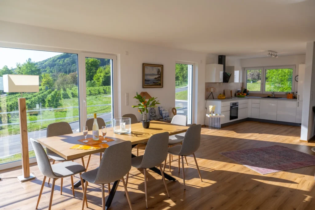 ferienhaus-aura-essbereich-esstisch-panoramafenster Essbereich im Ferienhaus Aura mit grossem Eichentisch fuer 6 Personen, offener Kueche und Panoramafenstern mit Blick auf Weinberge