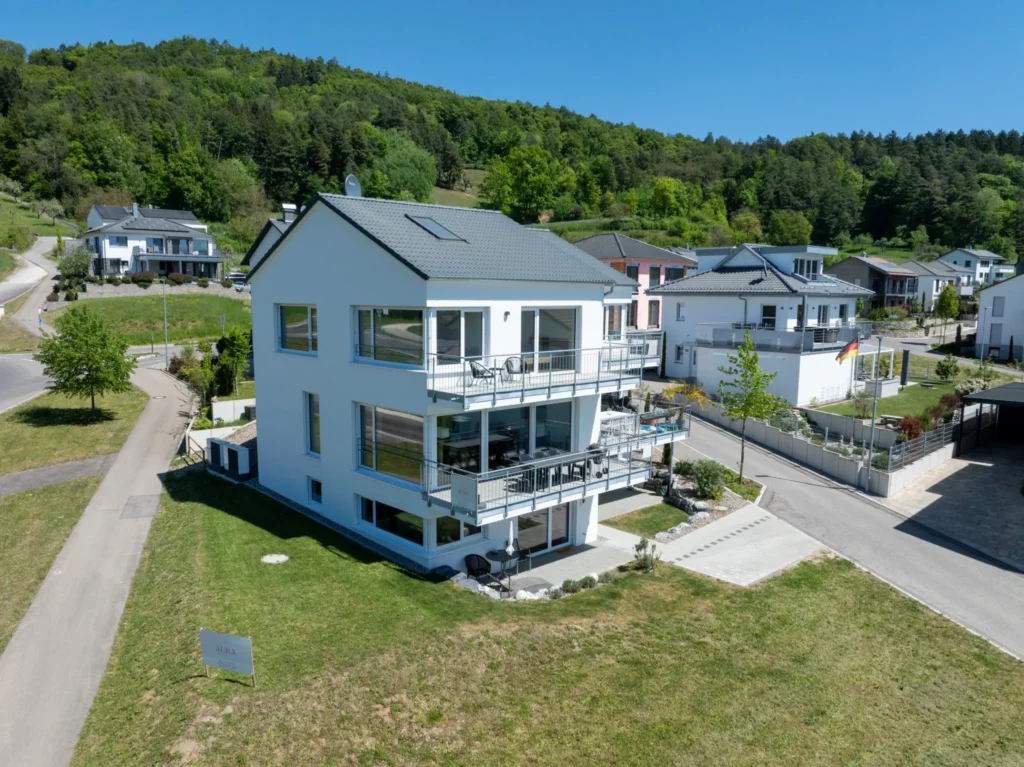 ferienhaus-aura-luftaufnahme-bodensee-vorderseite Luftaufnahme des Ferienhaus Aura am Bodensee - modernes weisses Dreifamilienhaus mit Balkonen, umgeben von gruenen Huegeln