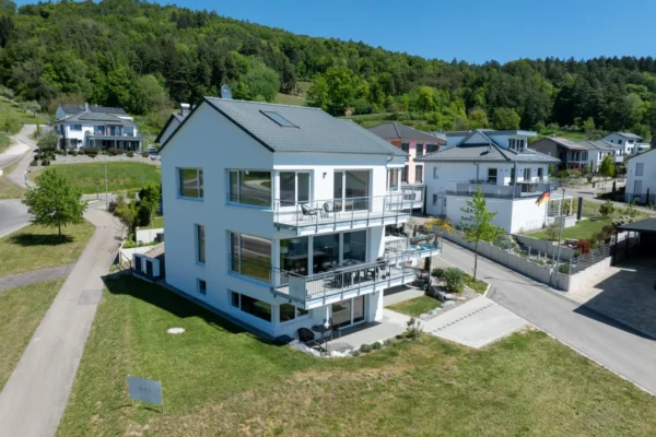Luftaufnahme des Ferienhaus Aura am Bodensee - modernes weisses Dreifamilienhaus mit Balkonen, umgeben von gruenen Huegeln