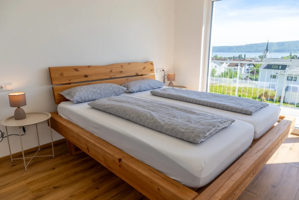 ferienhaus-aura-schlafzimmer-doppelbett-seeblick Schlafzimmer im Ferienhaus Aura mit Eichen-Doppelbett, Nachttischlampen und bodentiefen Fenstern mit Bodensee-Blick