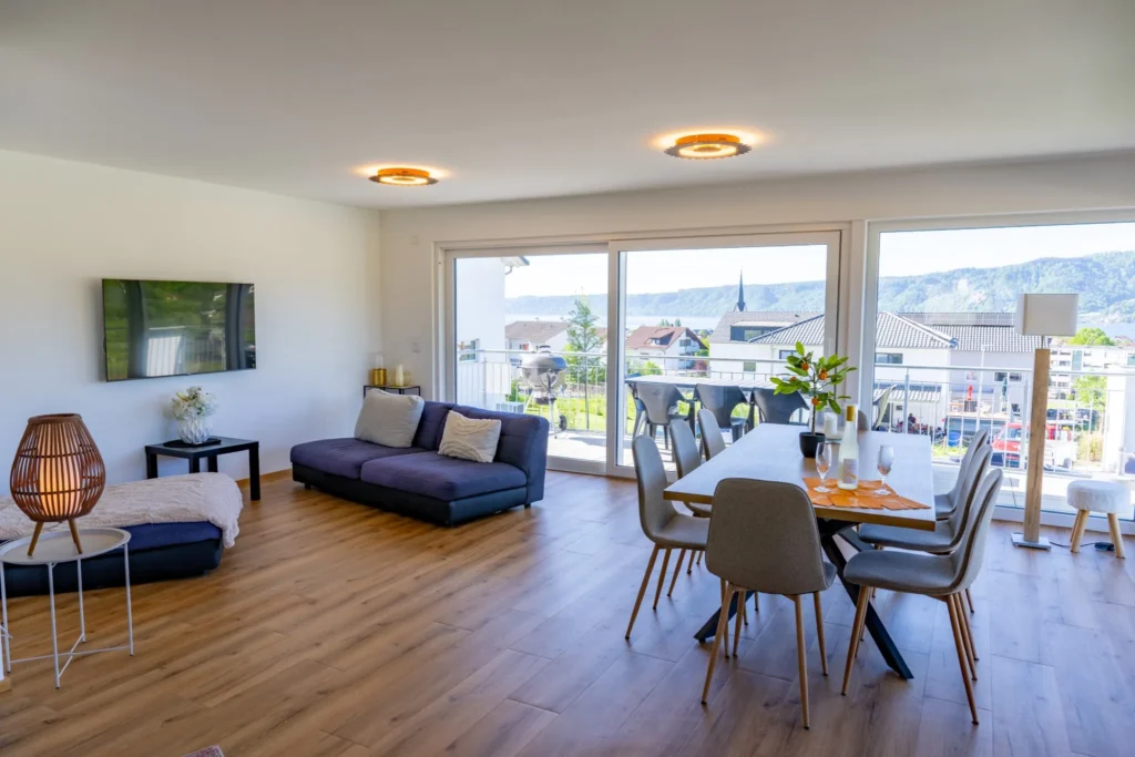 ferienhaus-aura-wohn-essbereich-panoramablick Grosszuegiger Wohn-Essbereich im Ferienhaus Aura mit Panoramafenstern, Seeblick und Designer-Beleuchtung