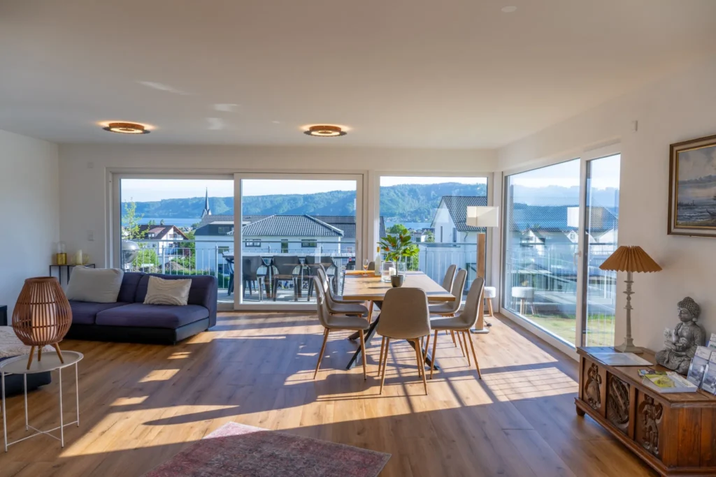 ferienhaus-aura-wohnbereich-panorama-bodensee Lichtdurchfluteter Wohnbereich im Ferienhaus Aura mit Panoramafenstern und Bodensee-Blick ueber die Daecher