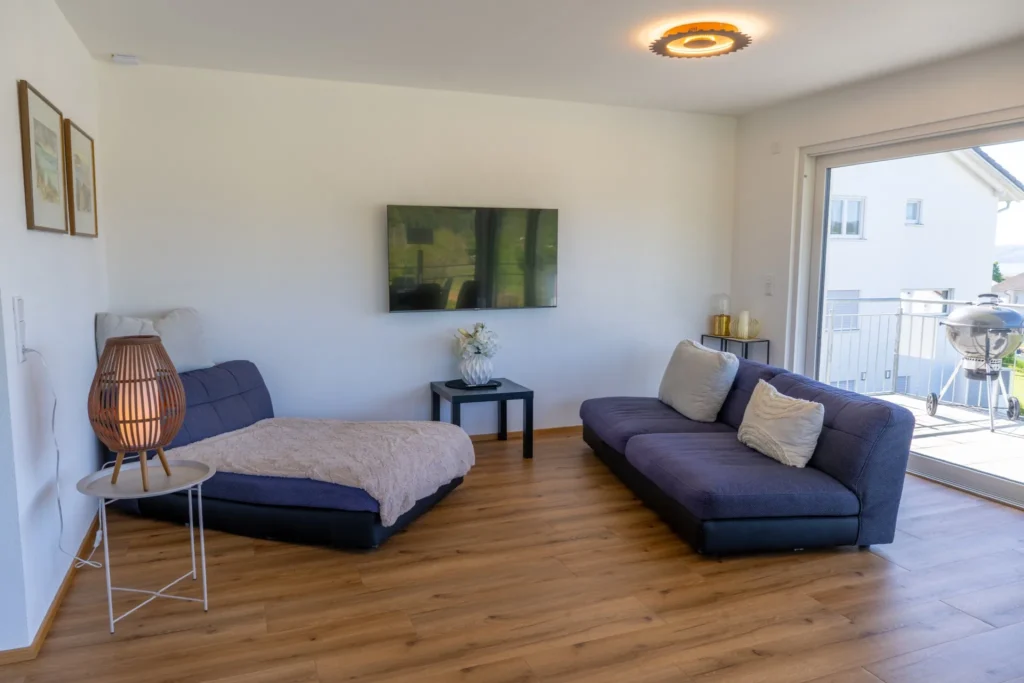 ferienhaus-aura-wohnzimmer-sofa-tv-balkonzugang Gemuetliches Wohnzimmer im Ferienhaus Aura mit L-foermigem Sofa, Wandfernseher und direktem Balkonzugang